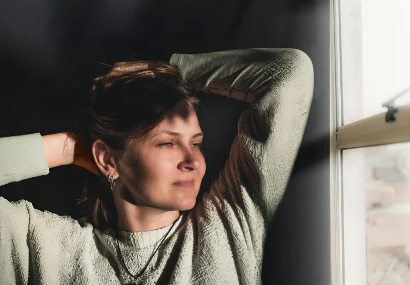 Femme sereine près d'une fenêtre dans la lumière naturelle, illustration de la stabilité retrouvée après une perte de poids