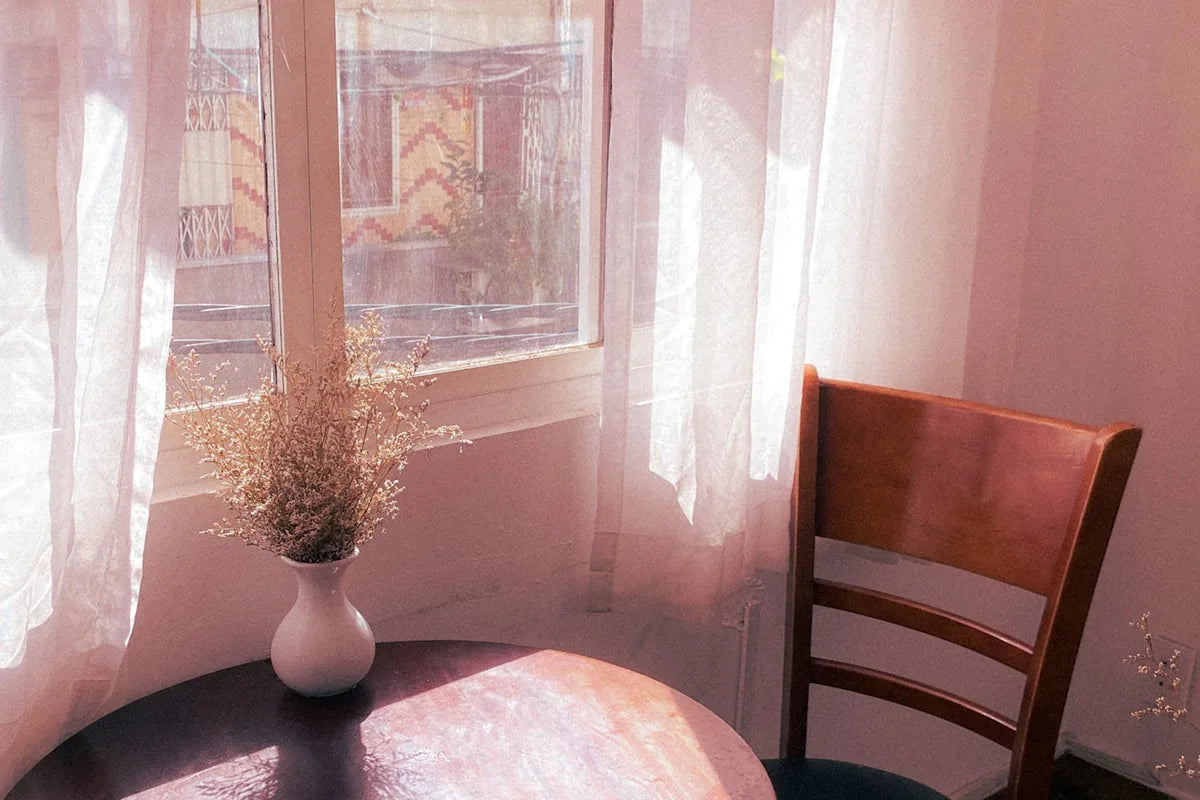 Table ronde près d'une fenêtre, chaise en bois, fleurs séchées - moment de pause face au plateau